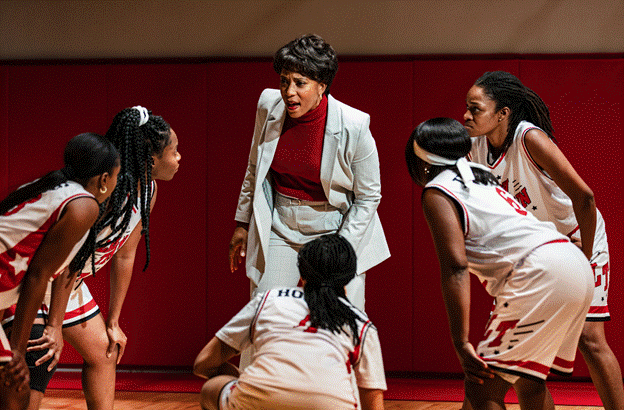 A person in a white suit and red shirt with a group of girls in the background

Description automatically generated