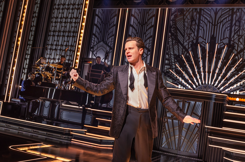 A person in a suit on stage
Description automatically generated