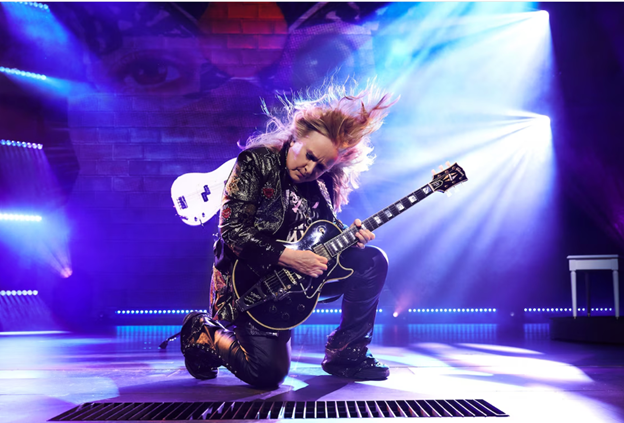 A person playing a guitar on a stage
Description automatically generated