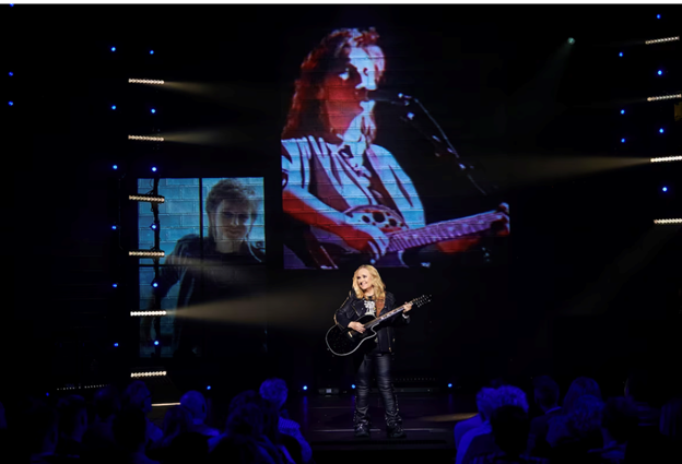 A person on a stage playing a guitar
Description automatically generated