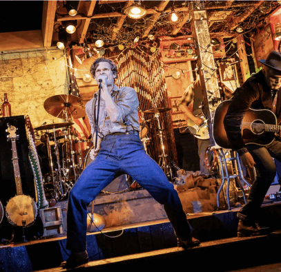 A person singing into a microphone on a stage with a person playing guitar

Description automatically generated