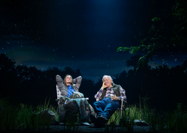 Two men sitting in chairs outside at night

Description automatically generated