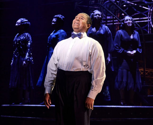 A person in a bow tie and bow tie standing on a stage
Description automatically generated