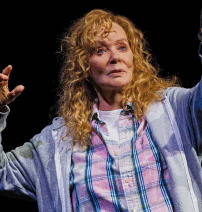 A person with curly hair and a grey sweatshirt with her hands up

Description automatically generated