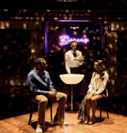 A person standing behind a person sitting on a stage

Description automatically generated