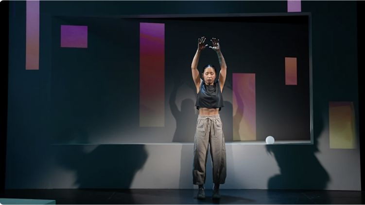 A person on stage with her hands up

Description automatically generated