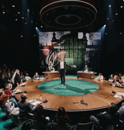 A person standing on a round table with people sitting in chairs

Description automatically generated