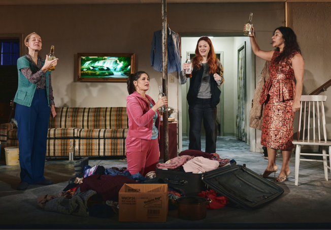 A group of women standing in a room with a suitcase and bottles of alcohol

Description automatically generated