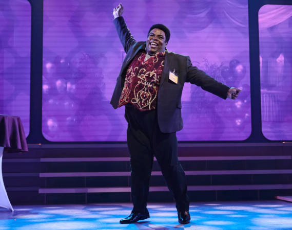 A person with his arms outstretched on a stage Description automatically generated