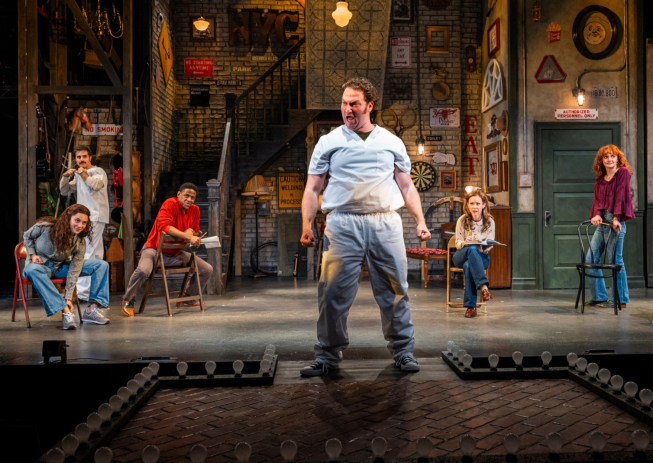 A person standing on a stage with people in the background Description automatically generated
