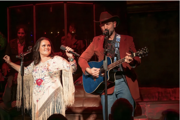 A person and person on stage with a microphone and guitar
Description automatically generated